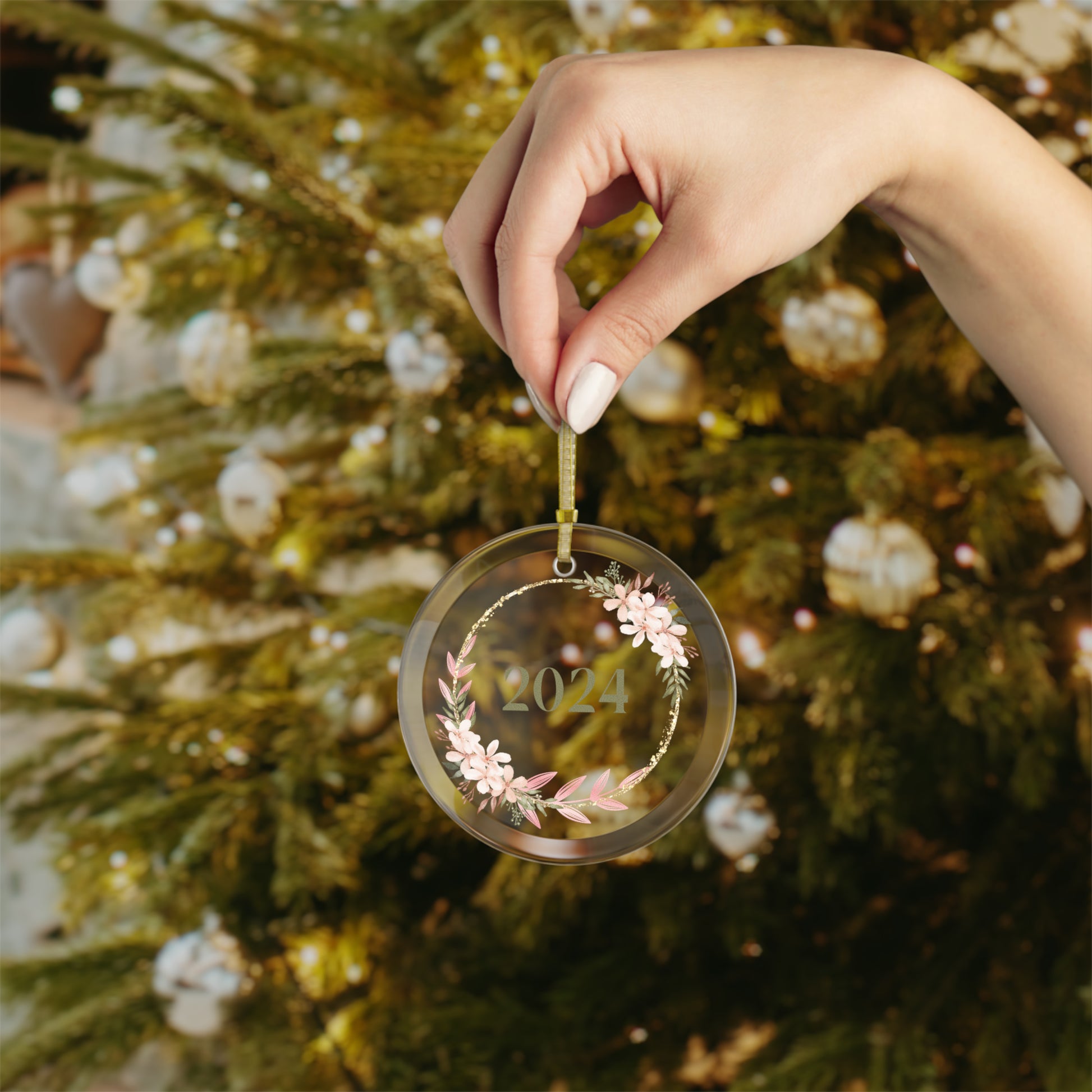 Hand holding Style 5 commemorative glass year ornament in front of Christmas Tree.