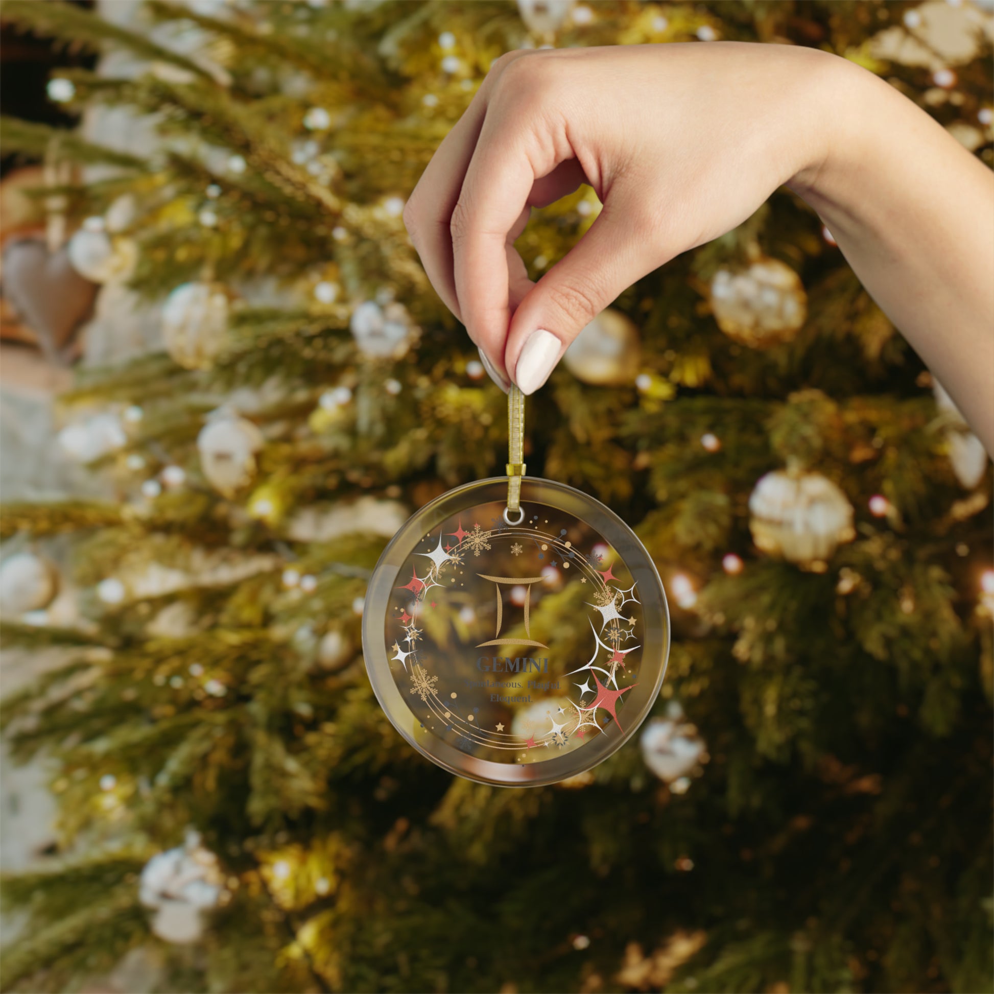 Hand holding glass zodiac ornament in front of Christmas tree.