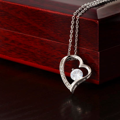 White gold heart pendant with cubic zirconia hanging over corner of mahogany jewelry box.