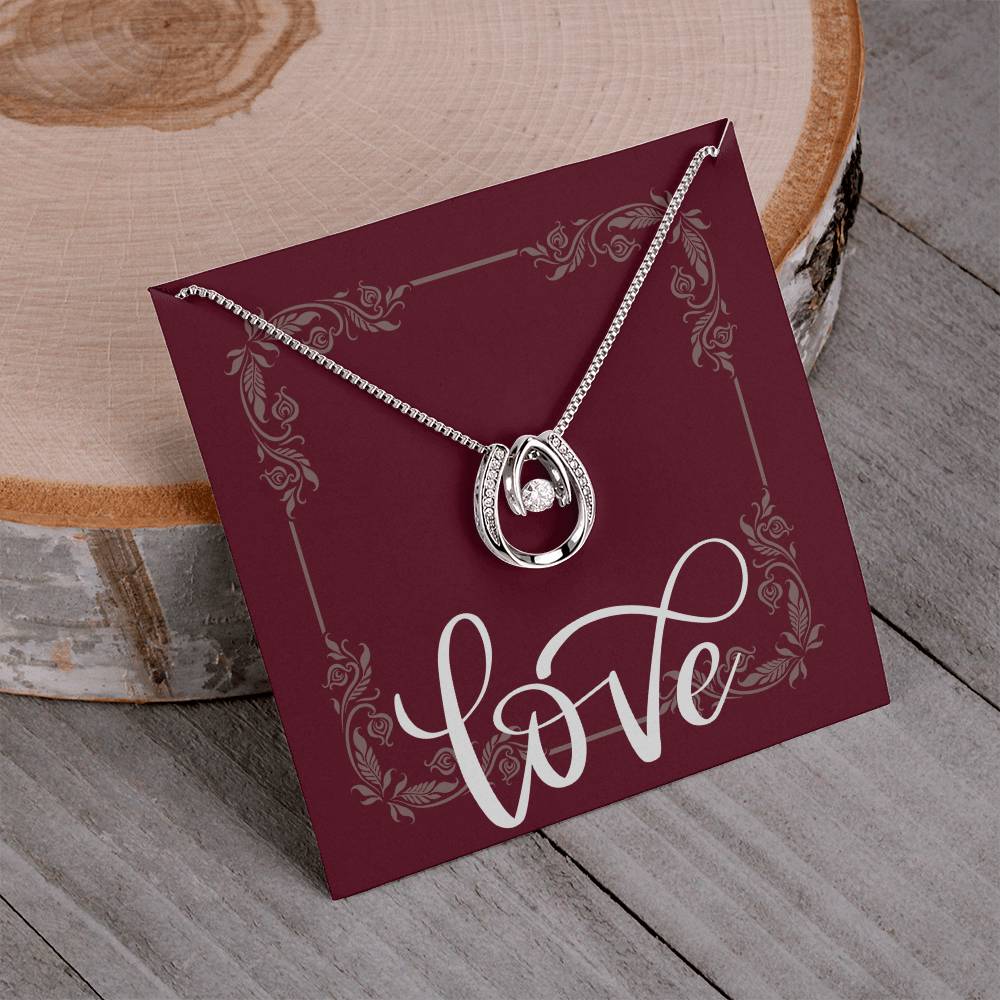 Lucky in Love necklace hanging around message card reading LOVE standing in front of wooden plate.