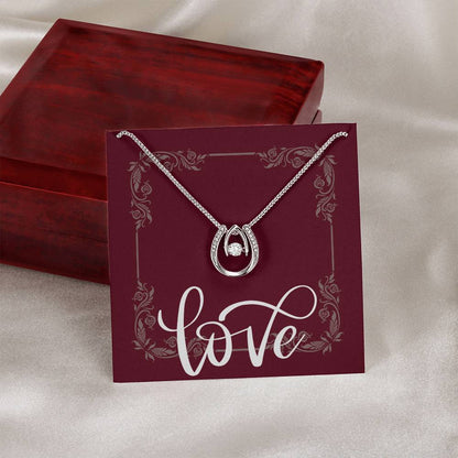 Lucky in Love pendant hanging around message card in front of mahogany jewelry box.