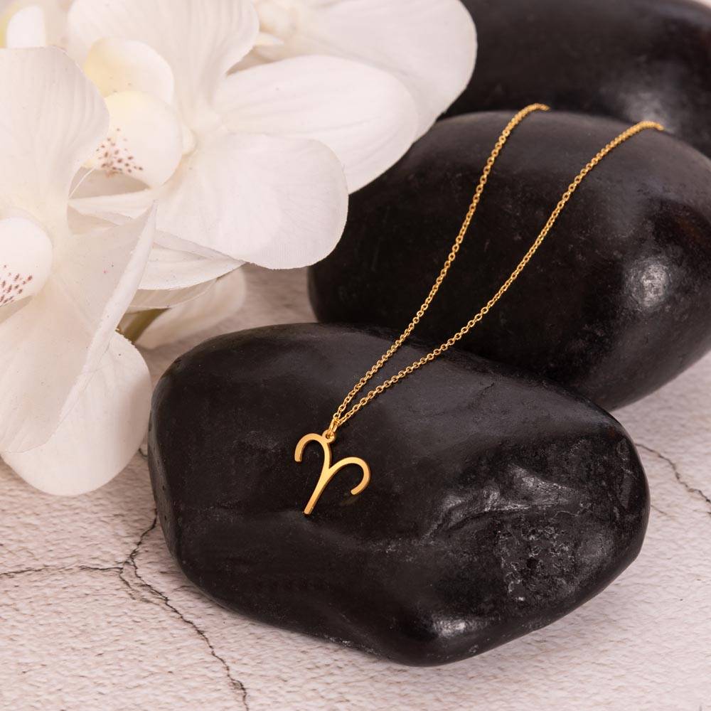 Gold zodiac charm necklace displayed on polished black rock.