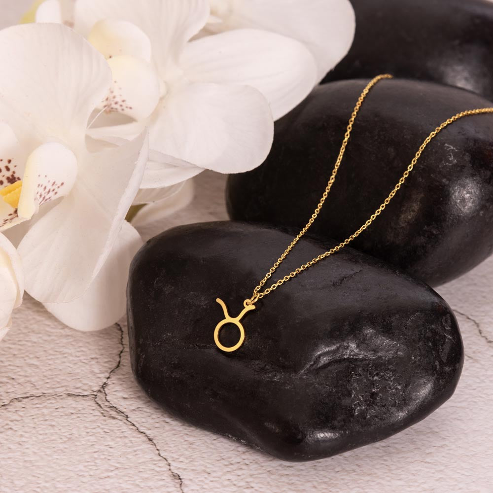 Gold zodiac charm necklace displayed on polished black rock.