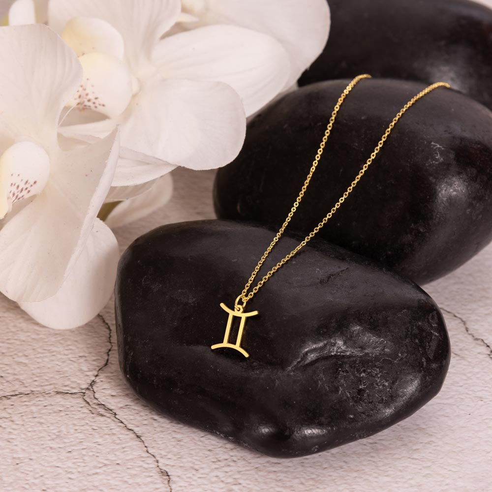 Gold zodiac charm necklace displayed on polished black rock.