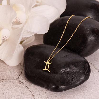 Gold zodiac charm necklace displayed on polished black rock.