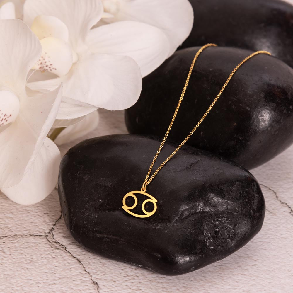 Gold zodiac charm necklace displayed on polished black rock.