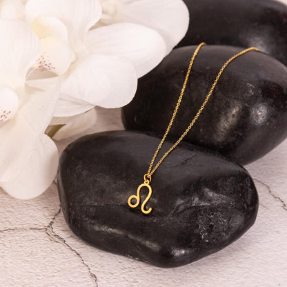 Gold zodiac charm necklace displayed on polished black rock.