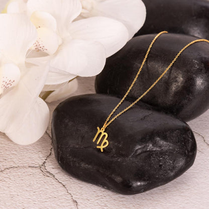 Gold zodiac charm necklace displayed on a polished black rock.