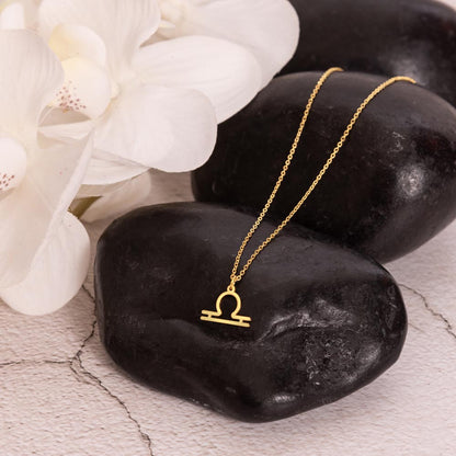 Gold zodiac charm necklace displayed on black polished rock.