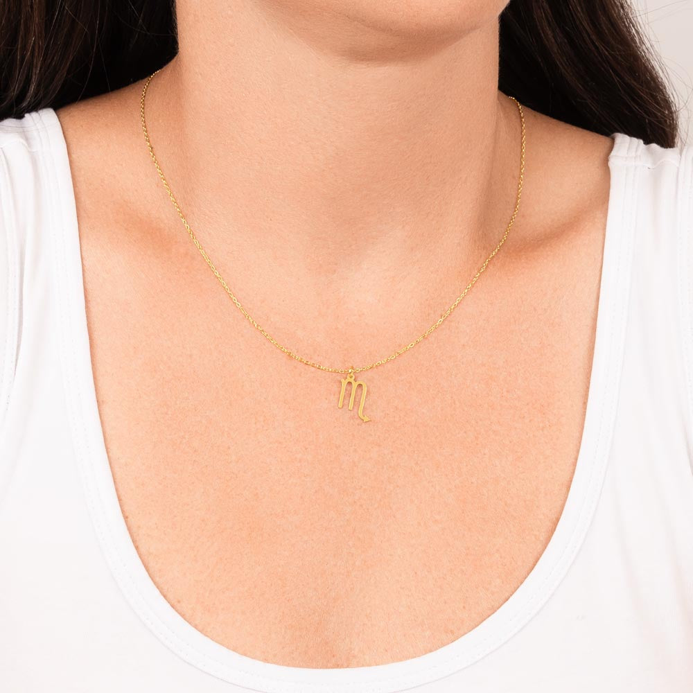 Gold zodiac charm necklace hanging around woman’s neck.