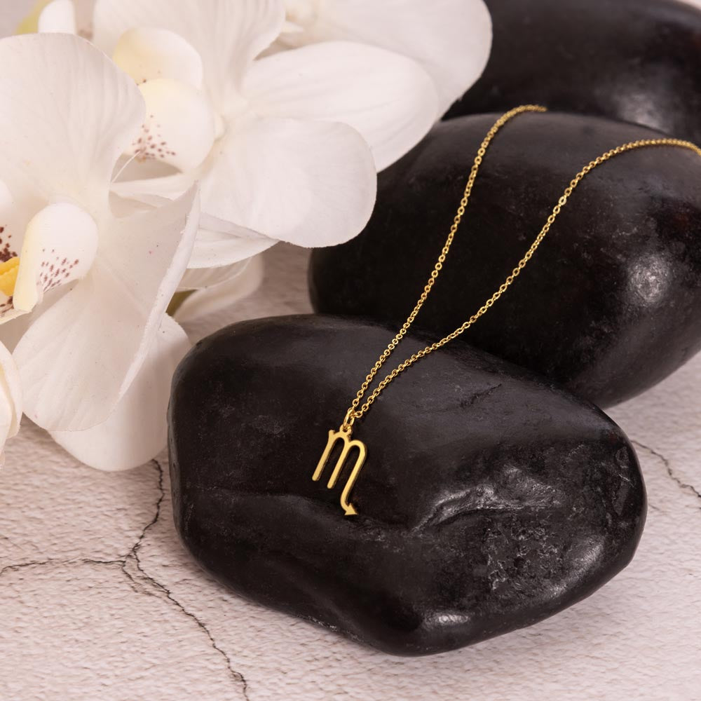 Gold zodiac charm necklace displayed on polished black rock.