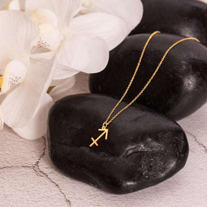 Gold zodiac charm necklace displayed on polished black rock.