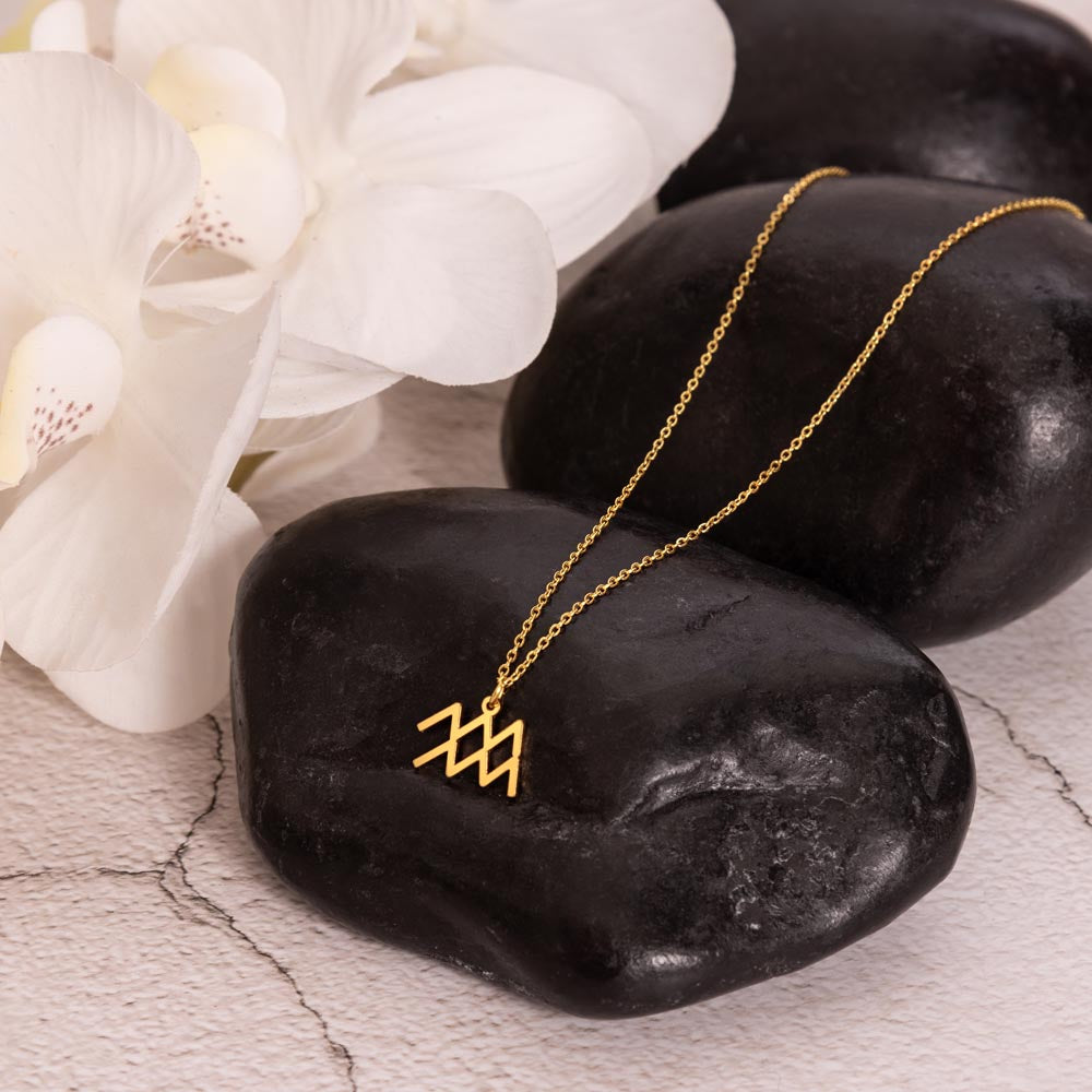 Gold zodiac charm necklace displayed on polished black rock.