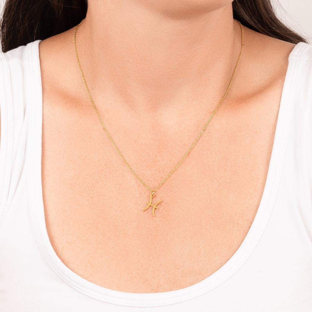 Gold Zodiac charm necklace hanging around woman’s neck.