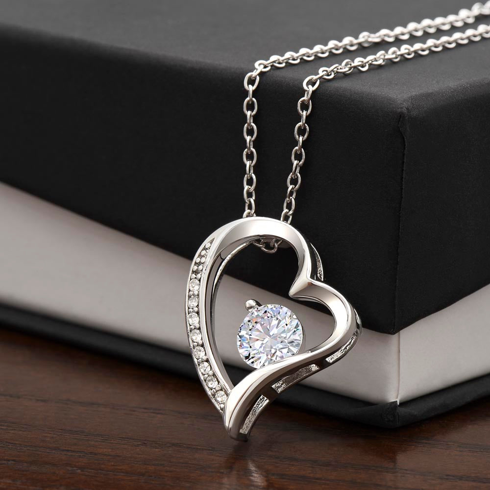 Polished white gold heart pendant with cubic zirconia hanging over corner of standard black box