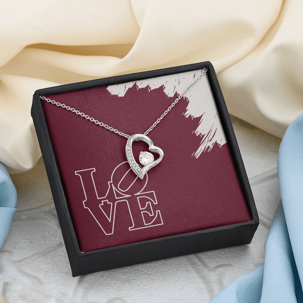 Polished white gold heart necklace in standard black box laying on silk fabric background.